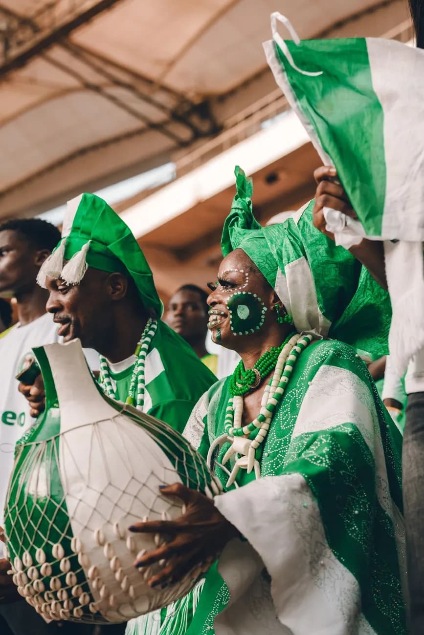 Celebrants in green and white Nigerian dress, one playing a shekere